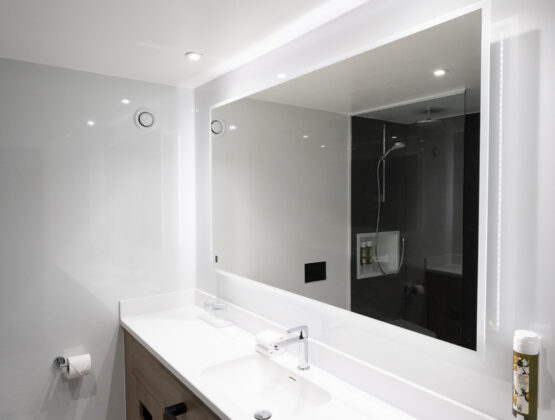A clean bathroom featuring a sink and a mirror above it, reflecting the room's bright lighting.
