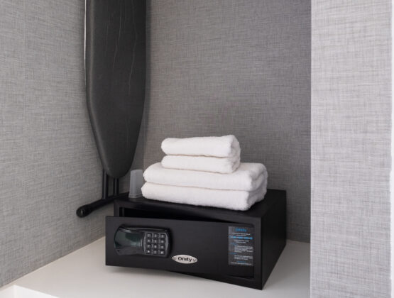 A closet space featuring an ironing board, a hotel room safe and spare towels.