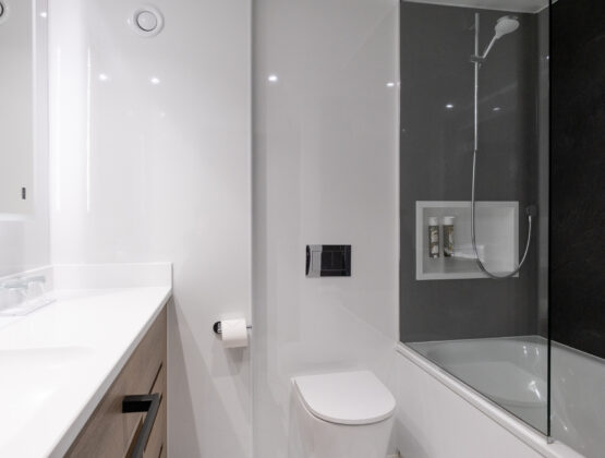 A clean bathroom featuring a toilet, sink, and shower, with neutral-colored tiles and bright lighting.