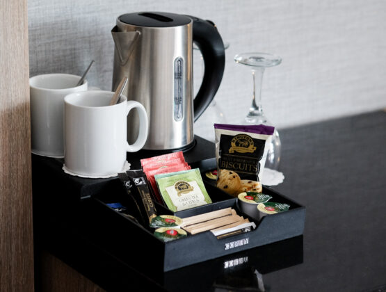 A tray containing complimentary coffee, tea, and snacks. Set up on the twin bedroom desk area, with a kettle and wine glasses.