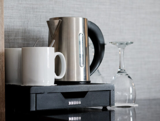 A kettle, two mugs and two glasses are placed on a desk, ready for brewing and serving coffee.